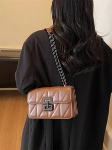 Brown quilted crossbody bag with metal chain strap and geometric clasp on model