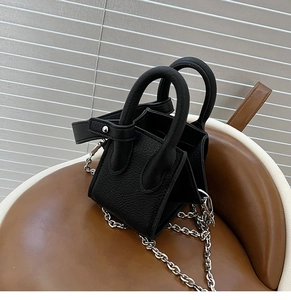 Detail of black pebbled leather bucket bag with silver chain strap and luggage style