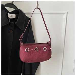 Detail of dark burgundy suede handbag with silver metal rings and rivets on white wall