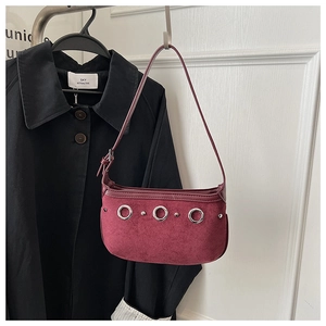 Detail of burgundy suede underarm bag with silver metal rings against a black jacket