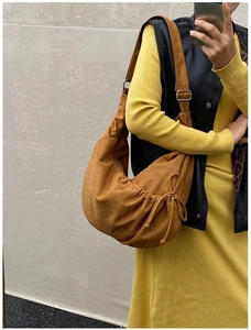 Detail view of caramel suede crescent bag featuring side drawstring pleats and metal buckles