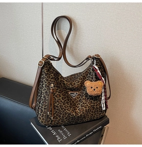 Detail of leopard print canvas shoulder bag with brown leather strap and plush bear charm