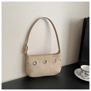 Close-up of beige suede shoulder bag featuring silver metal eyelets and adjustable strap