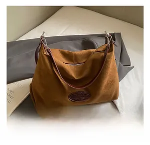Close-up of brown suede tote bag featuring an embossed oval logo and leather strap detail
