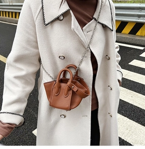 Detail of a brown lychee pattern leather mini bucket bag with silver chain on beige coat