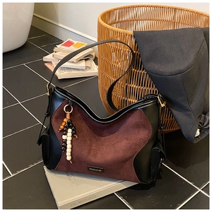 Detail of suede crossbody bag featuring logo plate and decorative beaded keychain charm