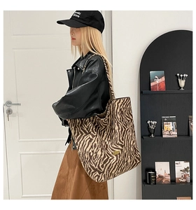 Model wearing a large leopard zebra print tote bag with gold logo in a modern home interior
