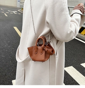 Outdoor street shot of a brown textured leather mini bucket bag with metal chain strap