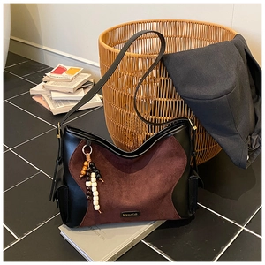 Close-up of black leather and burgundy suede handbag with beaded charm accessory