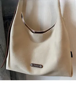 Close-up of beige canvas hobo bag featuring a leather logo patch and woven texture