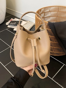 Minimalist beige drawstring bucket bag in textured pebble leather with gold hardware