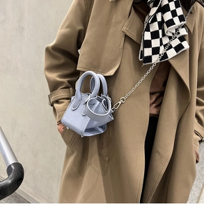 Close-up of light blue litchi leather mini bucket bag with silver chain on khaki trench coat