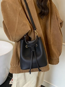 Minimalist black pebble leather drawstring bucket bag with gold hardware worn by model