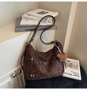 Detail of leopard print tote bag with brown leather strap and plush bear charm