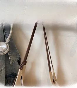 Detail of a brown leather shoulder strap with neat stitching on a beige canvas tote bag