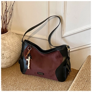 Detail of burgundy suede tote with bead charm and side pocket on textured carpet