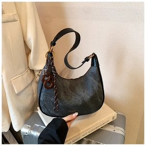 Detail of grey washed crescent bag with leather strap and decorative charms on a suitcase