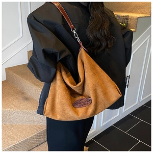 Detail of soft brown suede tote featuring leather shoulder strap and oval logo patch