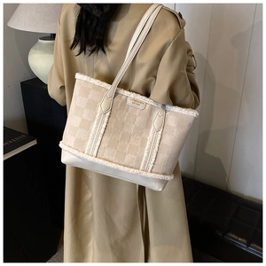 Detail of beige quilted tote bag with faux fur trim held by a model in a camel coat
