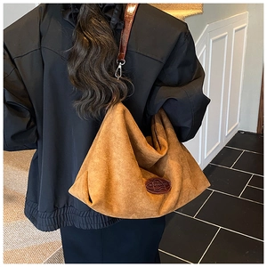 Detail of large brown suede hobo bag featuring oval logo patch and metallic hooks