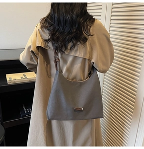 Detail of grey half-moon tote bag with brown straps worn by model in minimalist room