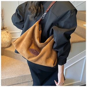 Macro shot of large caramel suede crossbody bag featuring embossed leather logo and silver hardware