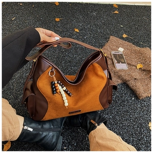 Detail of suede crossbody bag with vintage leather stitching and wood bead charm
