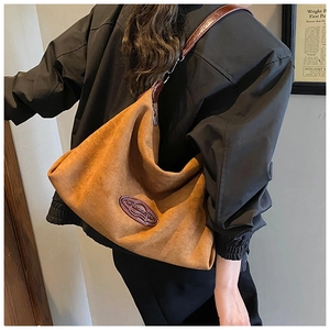 Detail of the brown suede hobo bag showing the leather logo patch and metal strap buckle