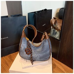 Detail of denim hobo bag with brown leather trim and unique pretzel shaped charm