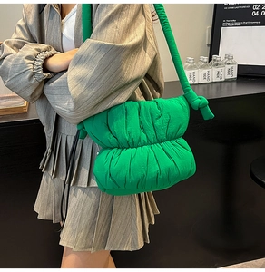Detail of a bright green puffy cloud bag featuring a wide knotted shoulder strap on a model