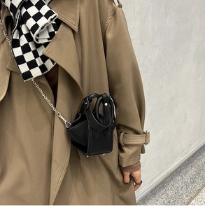 Detail of black pebbled leather bucket bag with silver chain strap and metal feet