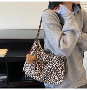 Detail view of leopard print tote bag with brown leather straps and plush bear charm
