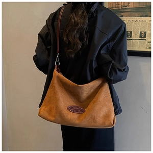 Caramel suede tote bag with brown oval logo and metal buckle on the long shoulder strap