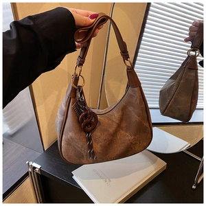 Detail of vintage brown crescent bag with woven charm and textured leather finish