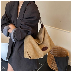 Detail of khaki suede tote bag showing the brown leather logo patch and shoulder strap texture