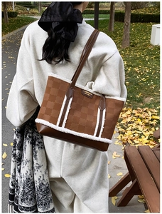 Detail of a brown embossed tote bag with faux shearling trim in a fall park setting
