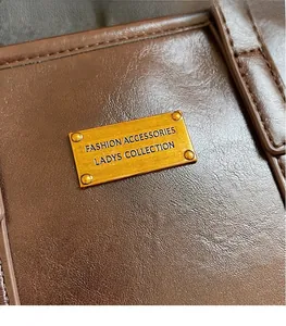 Close-up of brown lychee leather texture and golden metal logo plate on bucket bag