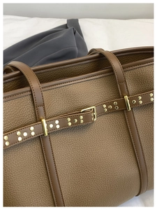 Detail of lychee pattern leather tote with gold rivets and buckle accents on dark brown bag
