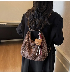 Detail view of leopard print tote bag featuring plush bear charm and woven tassel accent