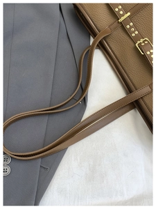 Detail shot of brown lychee leather tote bag with gold buckle and vintage metal rivets