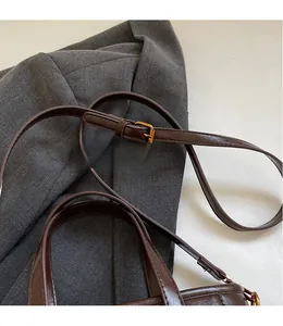 Detail of adjustable long shoulder strap with gold metal buckle on brown leather handbag