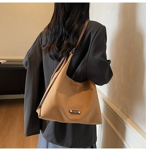 Detailed view of brown leather tote bag with silver logo plaque and adjustable shoulder strap