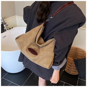 Detail of a large khaki suede tote bag showing soft texture and brown leather patch accent