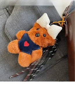 Detailed plush brown bear charm with white bow on a stylish brown leather bucket bag