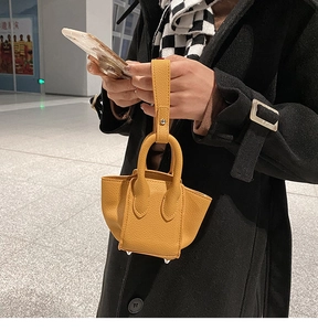 Detail of yellow pebble leather mini tote bag featuring metal bottom studs and hand strap