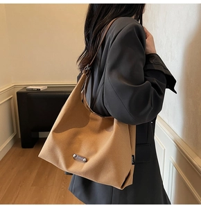 Side view of a brown minimalist hobo bag worn by a model in a grey blazer suit