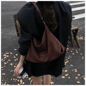 Detail of dark brown suede tote bag with vintage logo patch and red leather strap