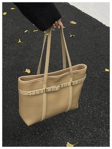 Detail of khaki pebbled leather tote bag with gold rivets and buckle on asphalt background