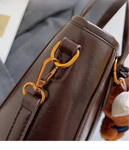 Detail of dark brown leather bucket bag with gold metal hardware and plush bear charm