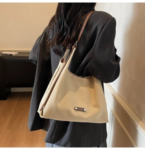 Detail of a large beige tote bag with brown leather straps worn by a model in a minimalist setting